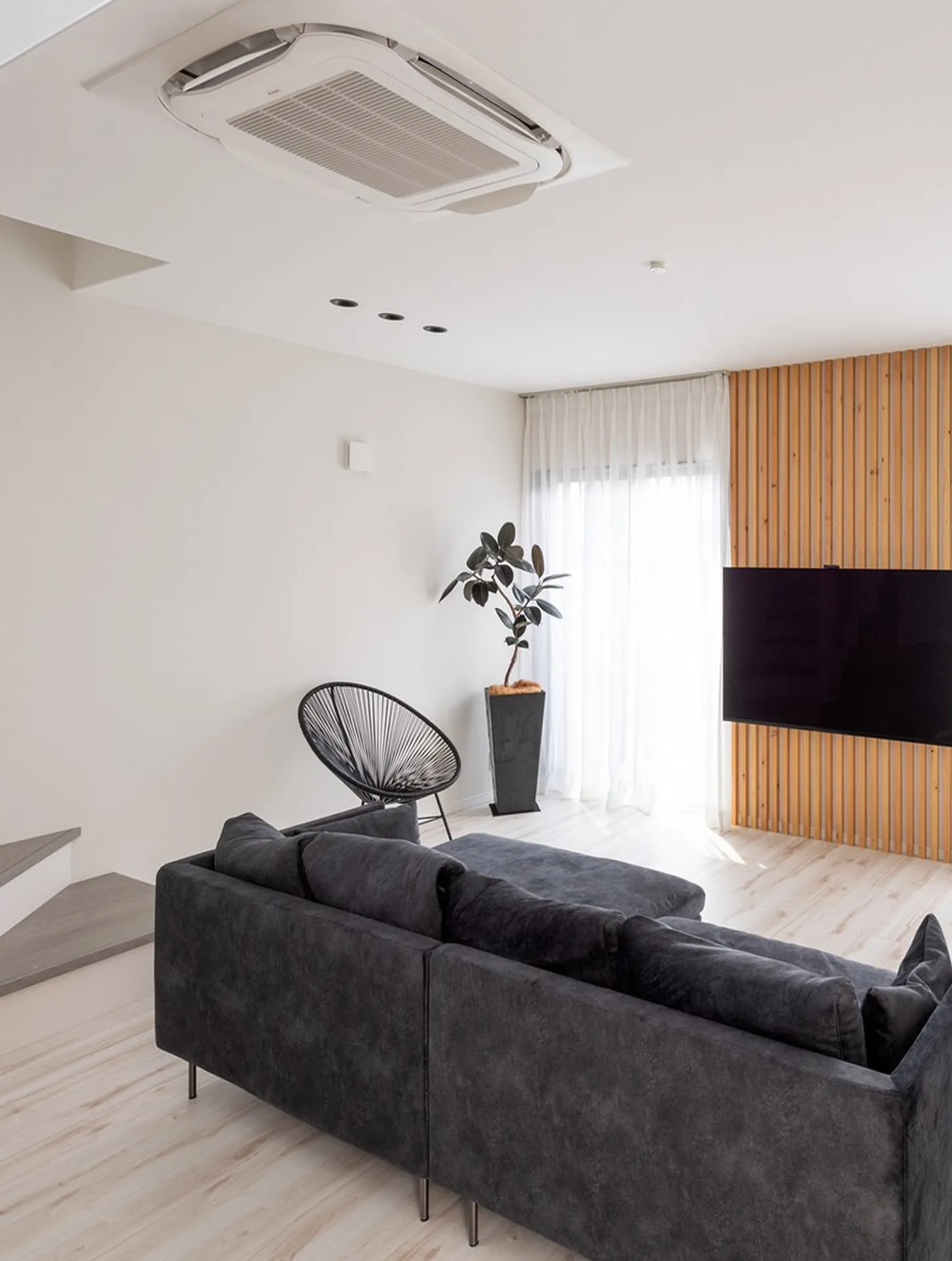 住宅リビングの施工事例｜木目パネルとグレーソファを基調にしたモダンな居住空間